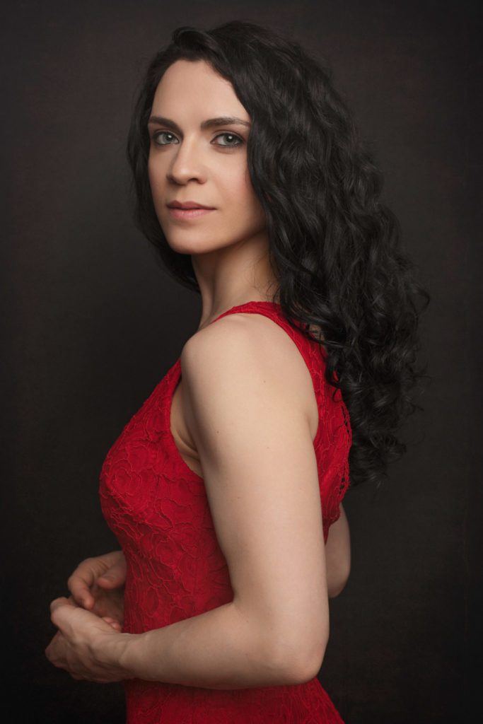 Retrato de estudio de una mujer de pelo rizado con vestido rojo, girada de perfil sobre fondo oscuro