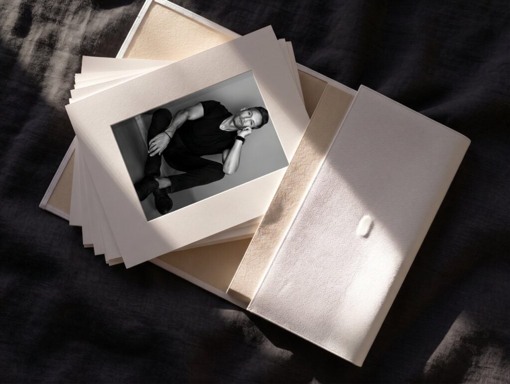 Photobox de cuero blanco abierto con fotografías en passepartout, sobre lino carbón